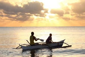 Two people rowing a boat at sunset in the Philippines 