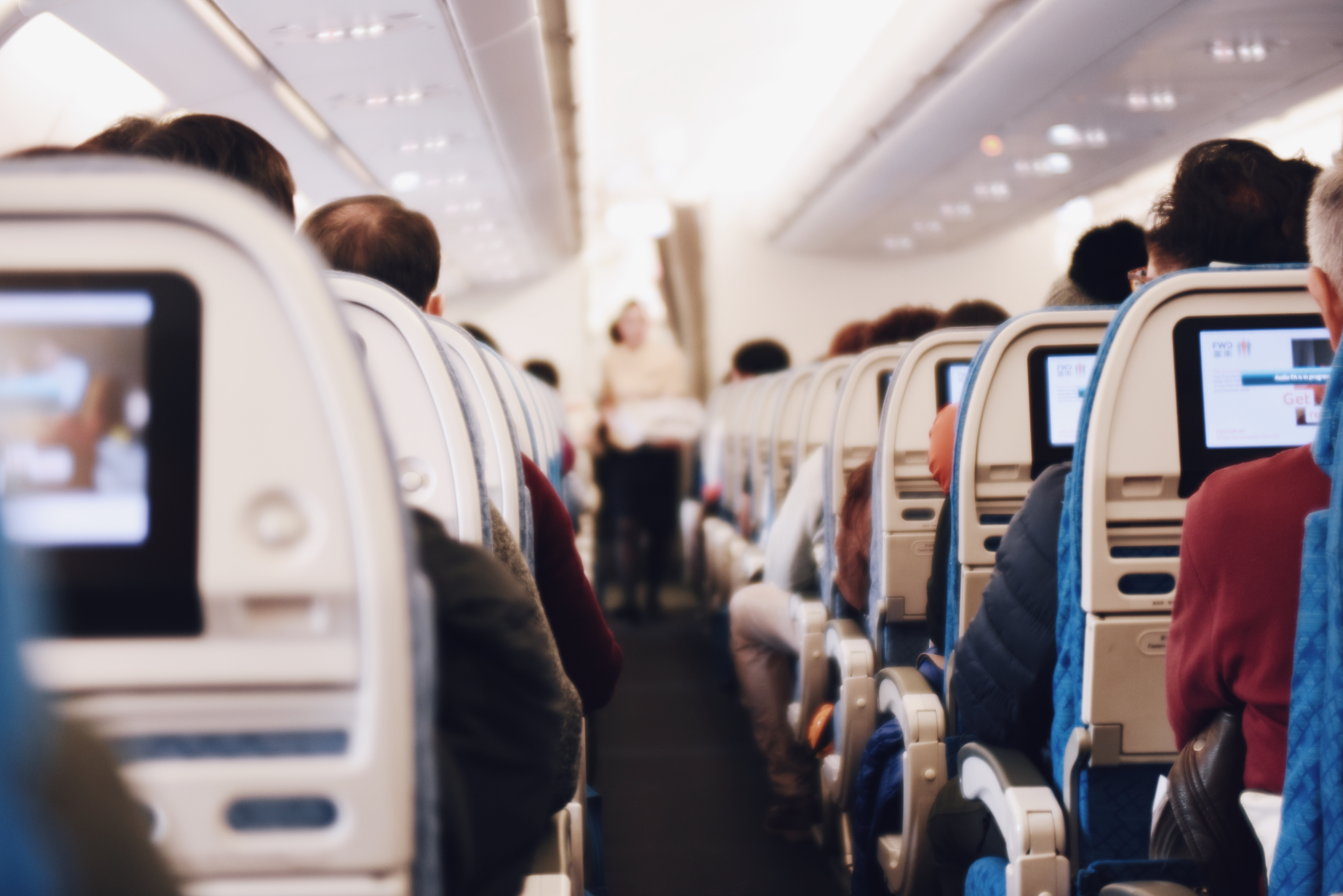 View from the aisle of a plane showing passengers sat in their seats and the flight attendant checking on them