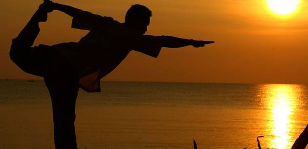 Person doing yoga by the sea at sunset