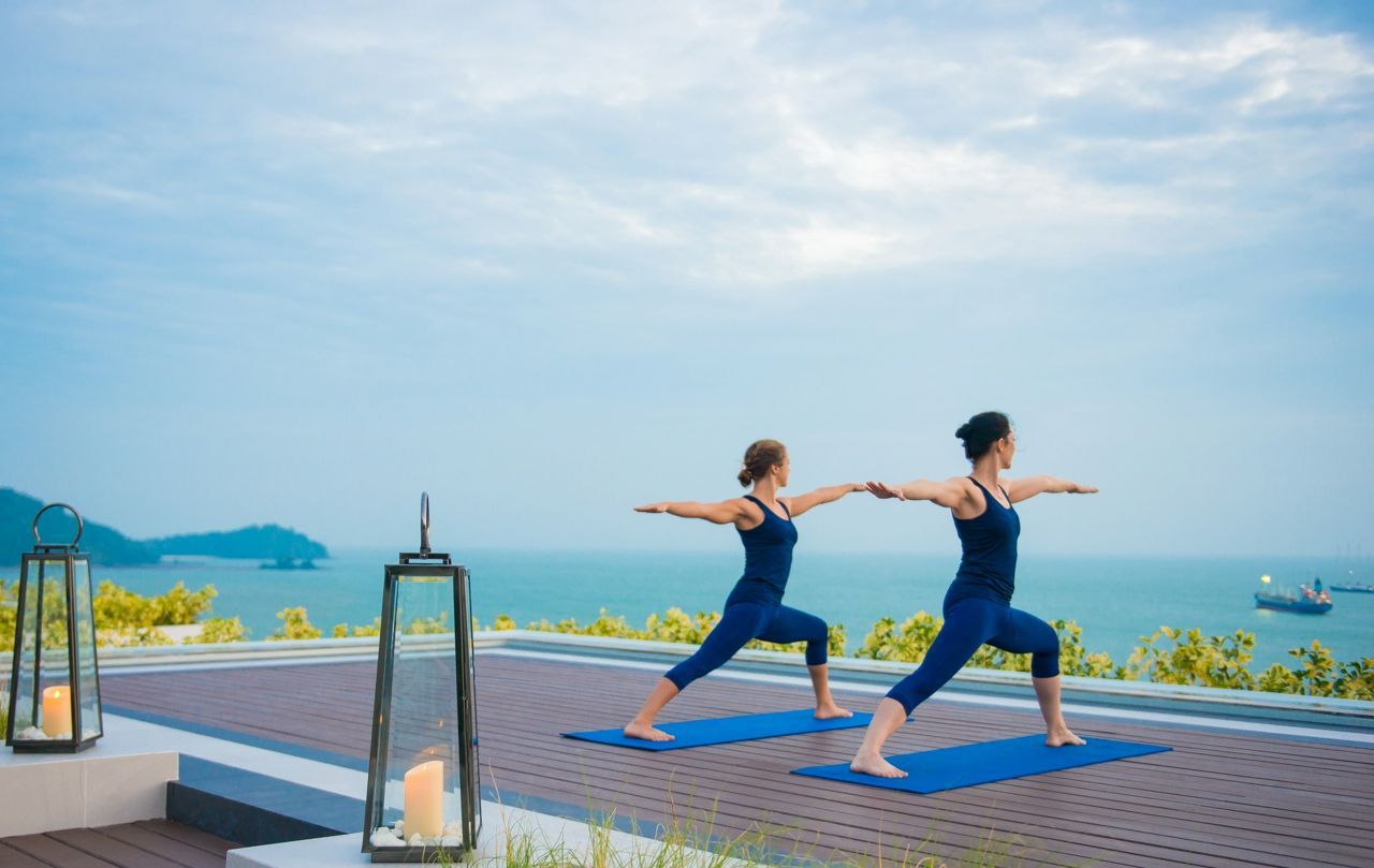 Two people practicing yoga by the sea