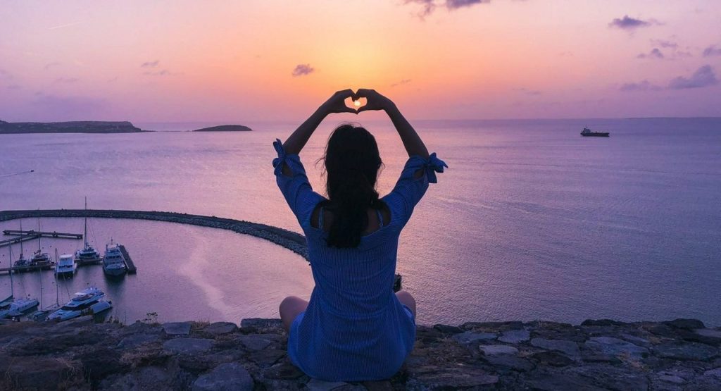 Woman sat on stone wall looking out over a bay.