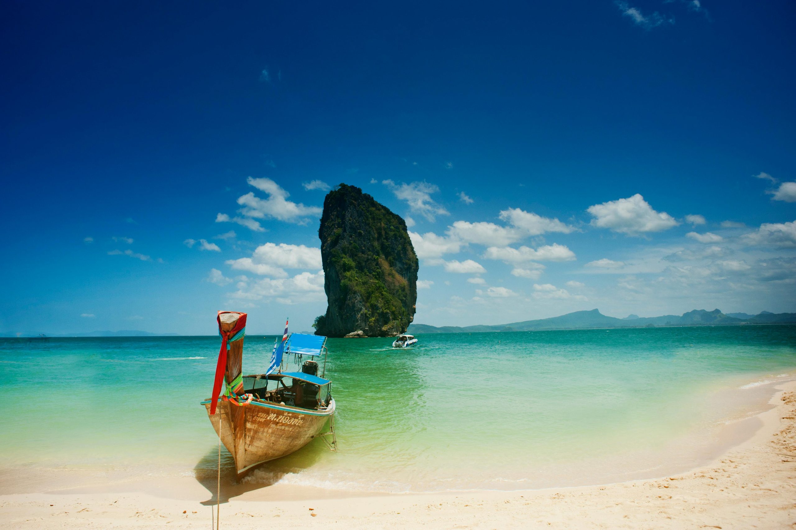 Boat on white sand beach with mossy rock.