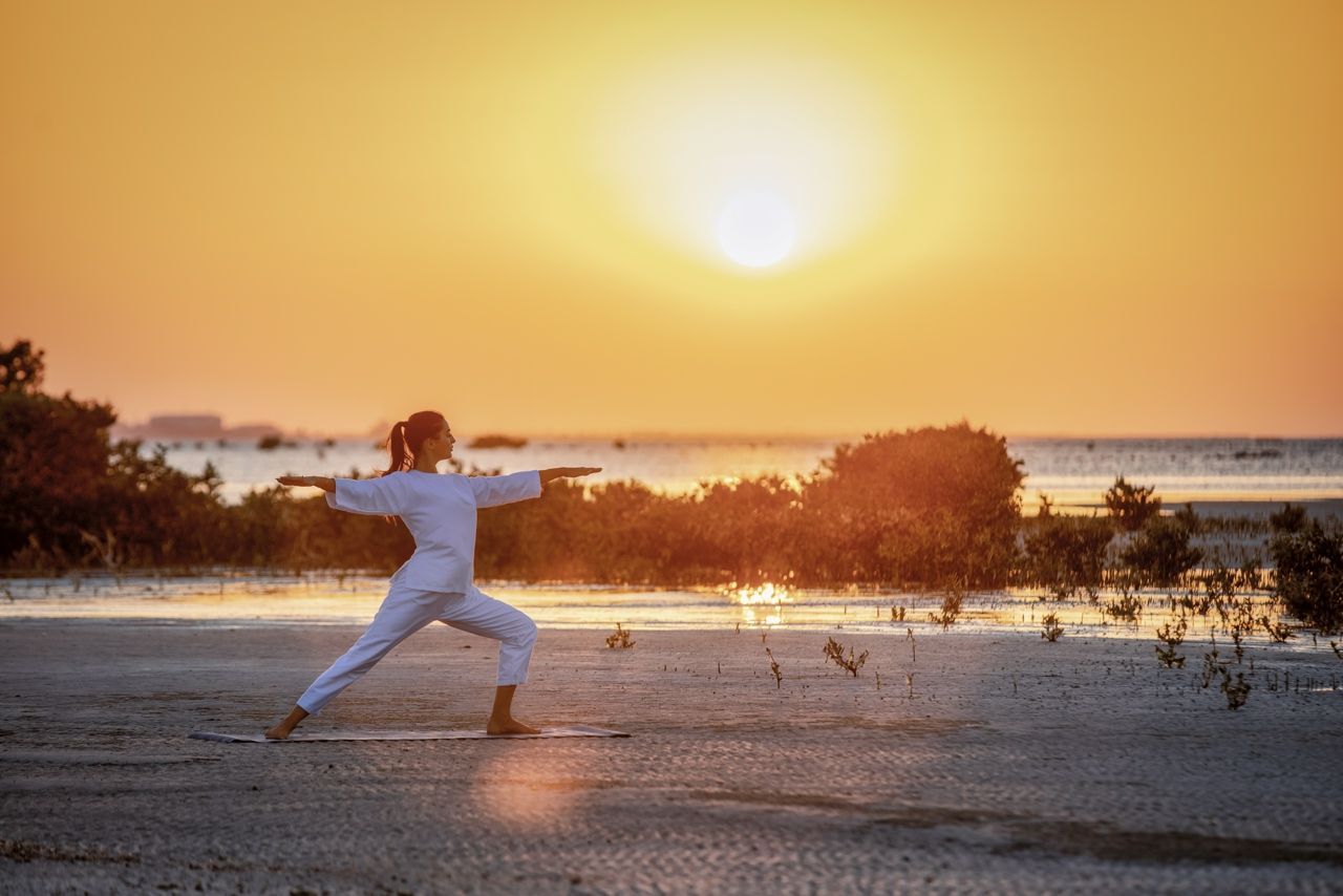 Woman practicing yoga on the beach at Zulal Wellness Resort in Qatar