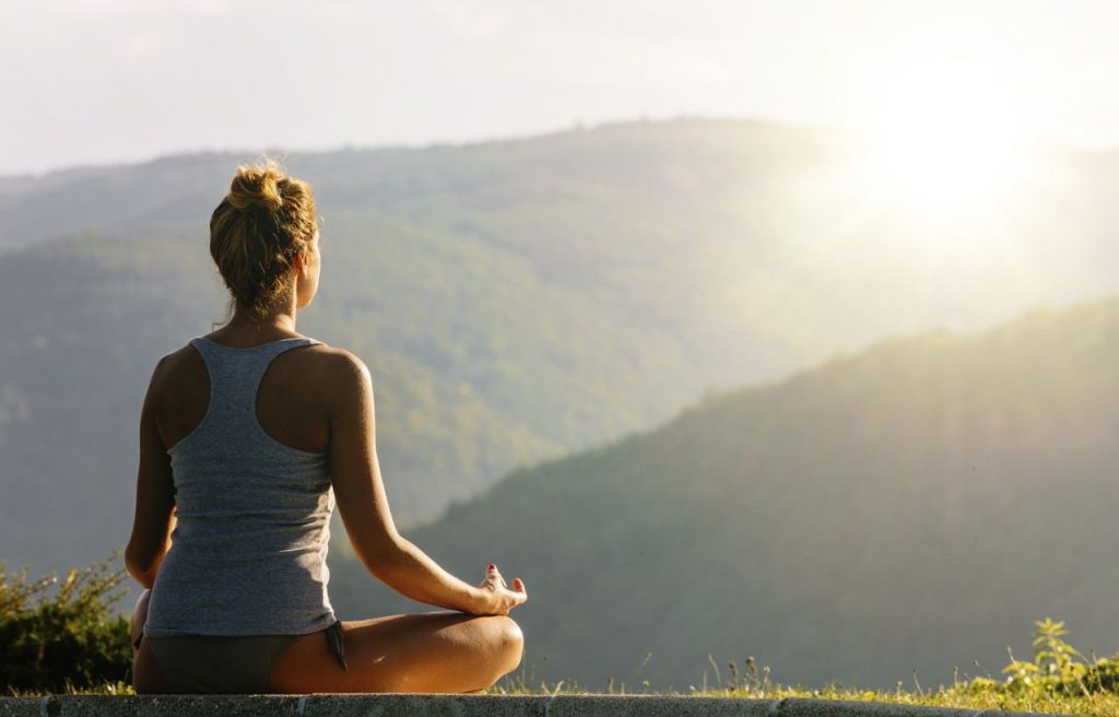 Young woman meditating on the high mountain and looking into sun